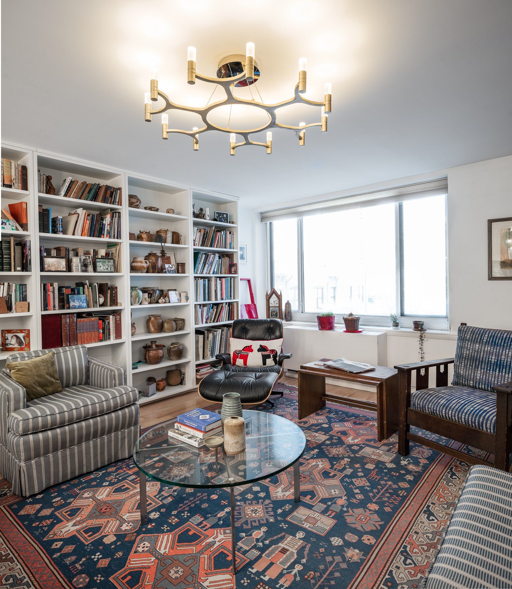 Living room with built-in bookshelves, large window, and modern gold ceiling light