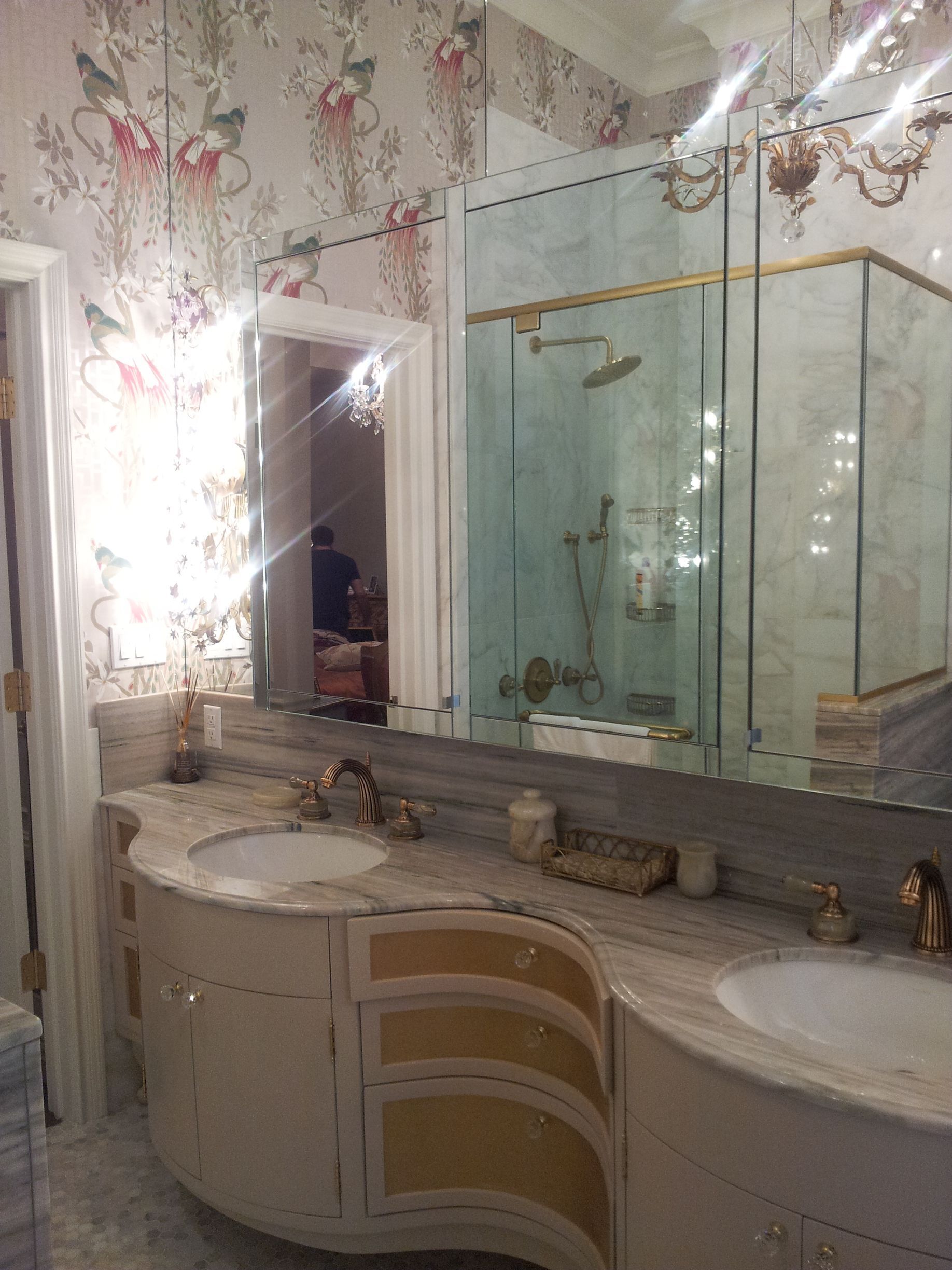 Elegant bathroom with floral wallpaper, glass shower enclosure, brass trim, and chandelier