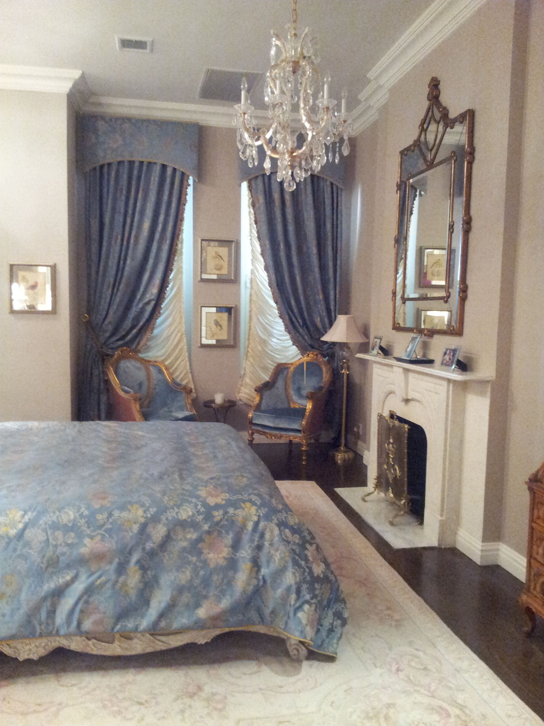 Elegant bedroom with crystal chandelier, blue drapery, ornate mirror, and classic wall molding
