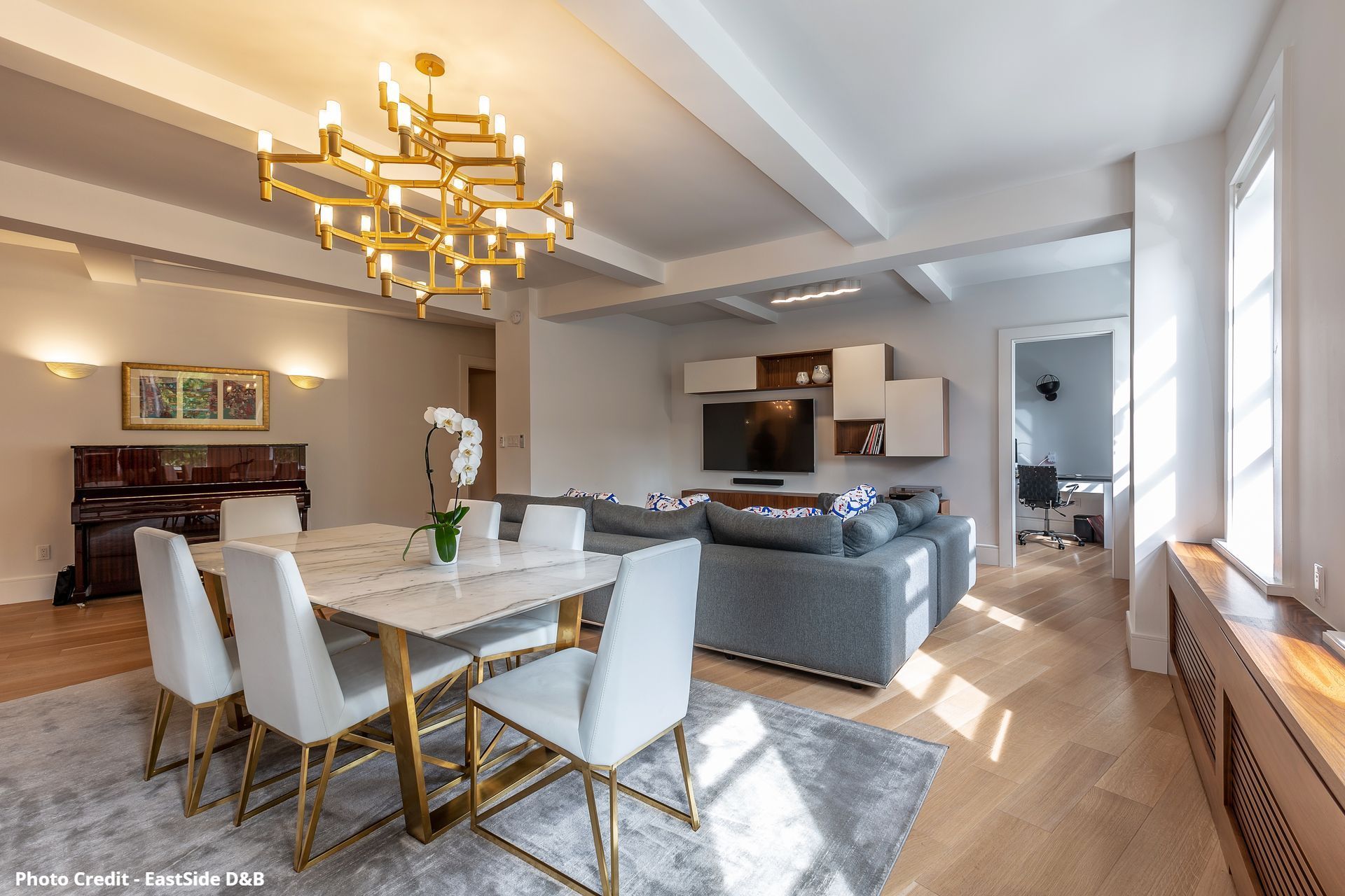 Open living and dining room with gold chandelier, dining table, sofa, and warm natural light
