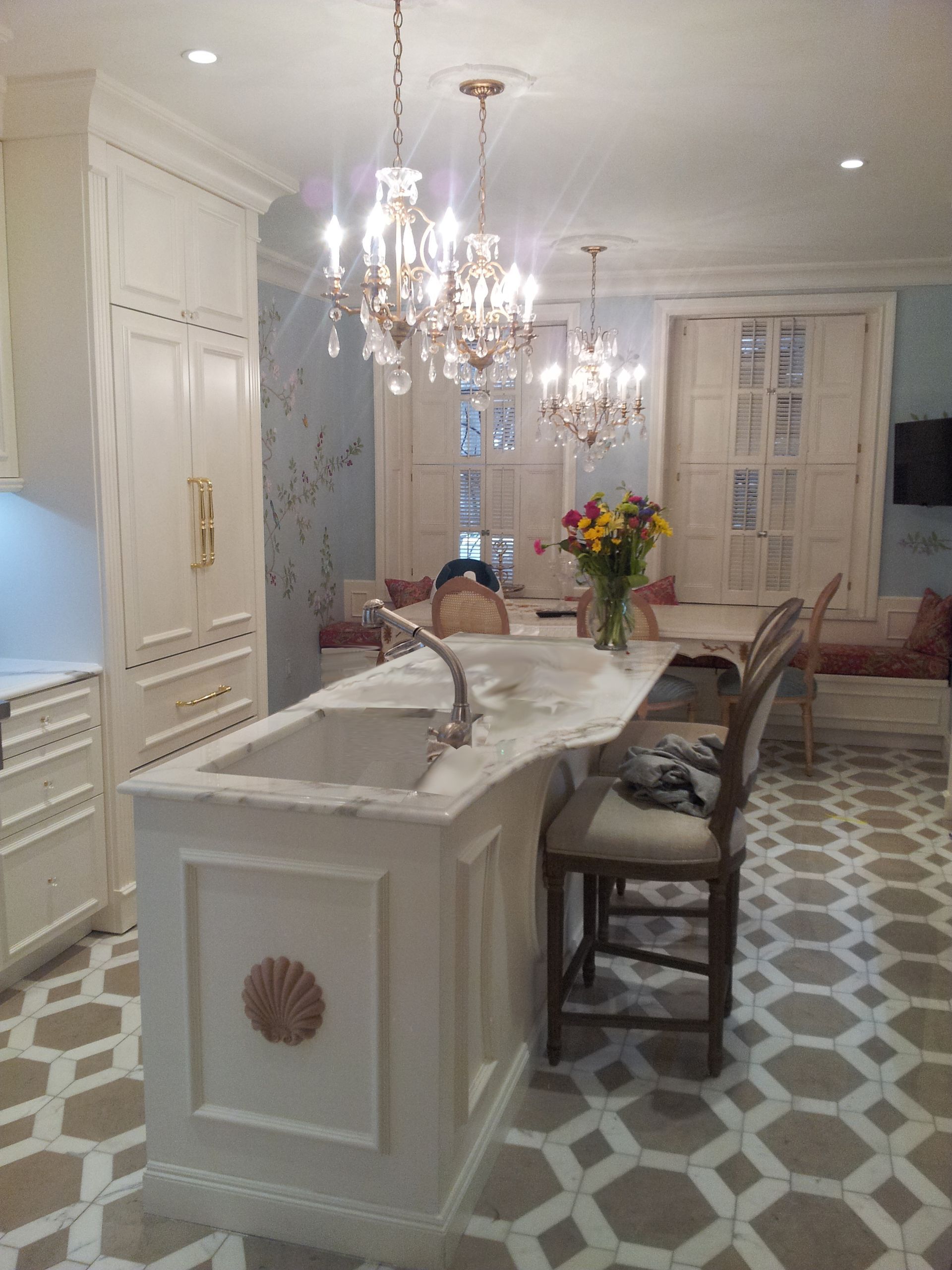 Elegant kitchen or dining area with crystal chandelier, white cabinetry, and floral wallpaper
