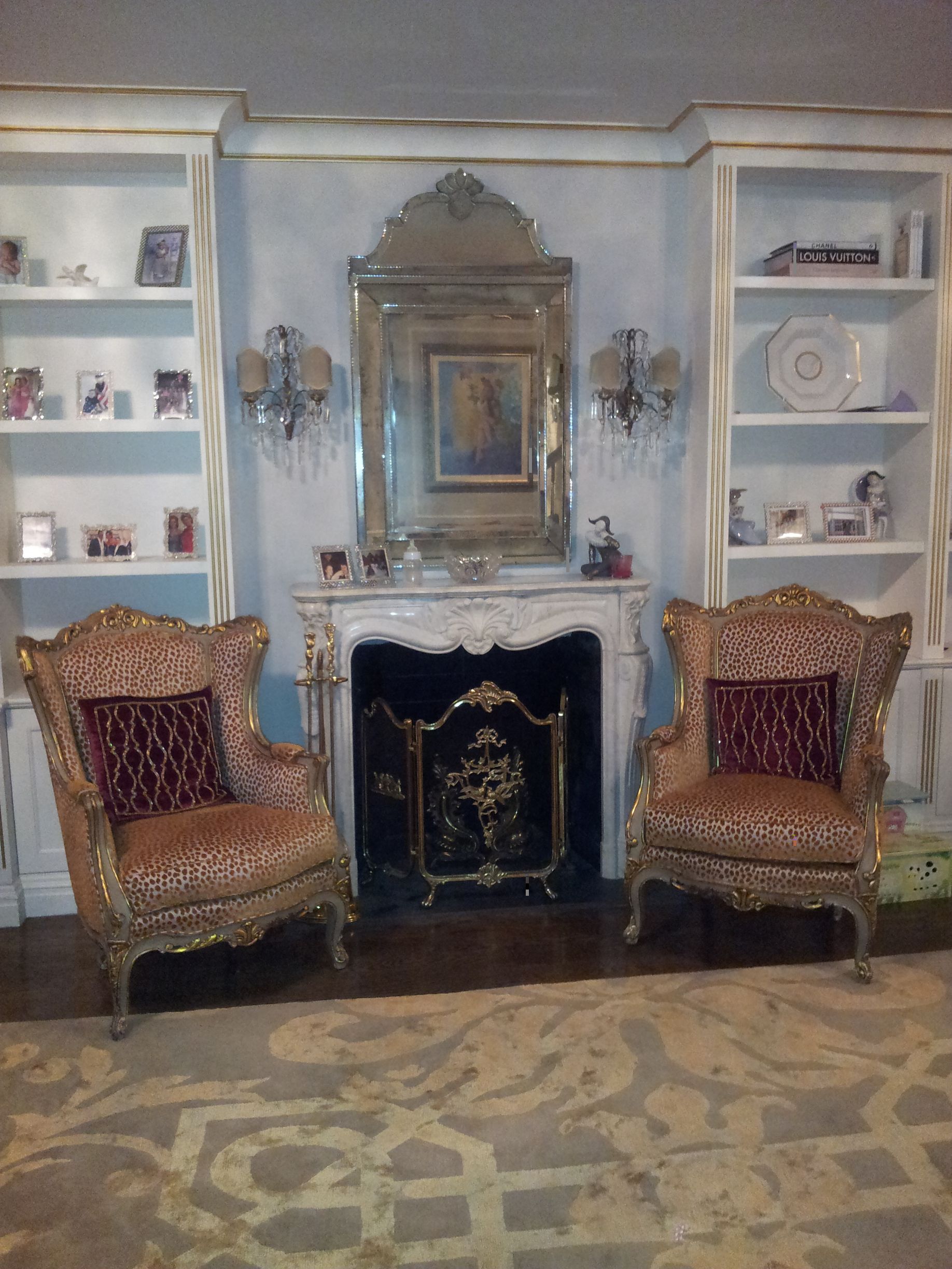 Living room Elegant wall display with ornate mirror, sconces, built-in shelves, photos, and decorative objects, and a marble fireplace 
