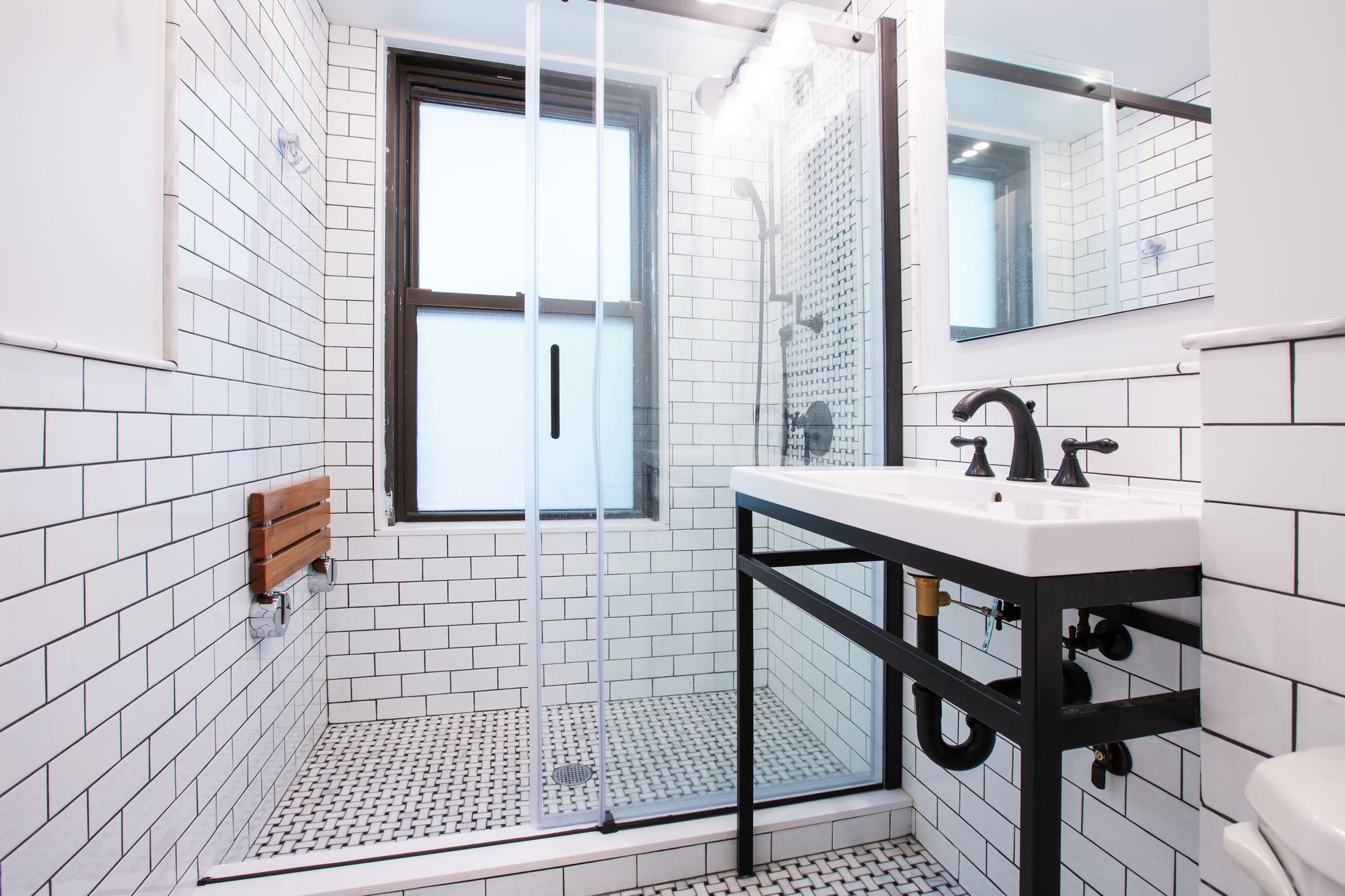 White subway tile bathroom with black-framed shower, vanity, and window