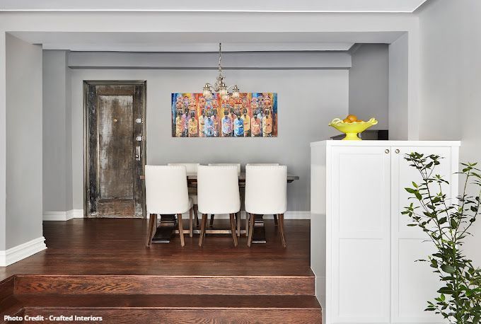 Elegant dining area with white chairs, colorful wall art, dark wood floor, and modern sideboard