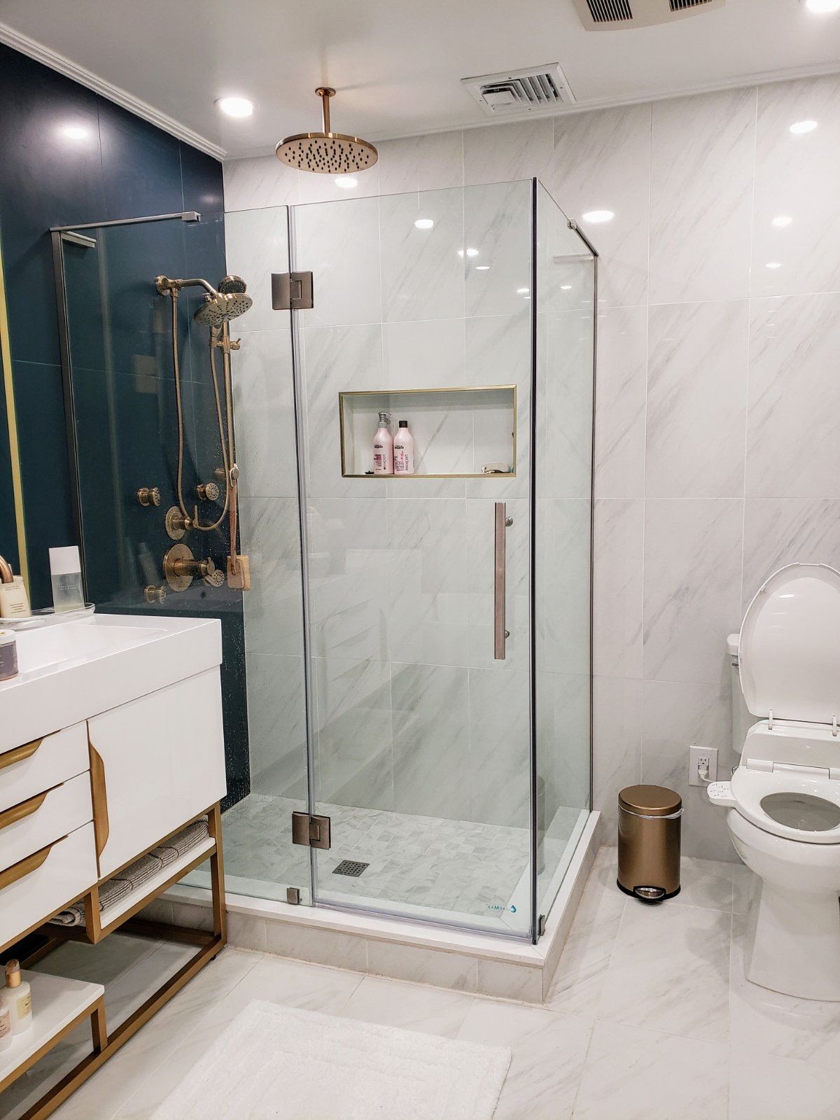 Modern glass shower with navy accent wall, brass fixtures, recessed niche, and marble-look tile