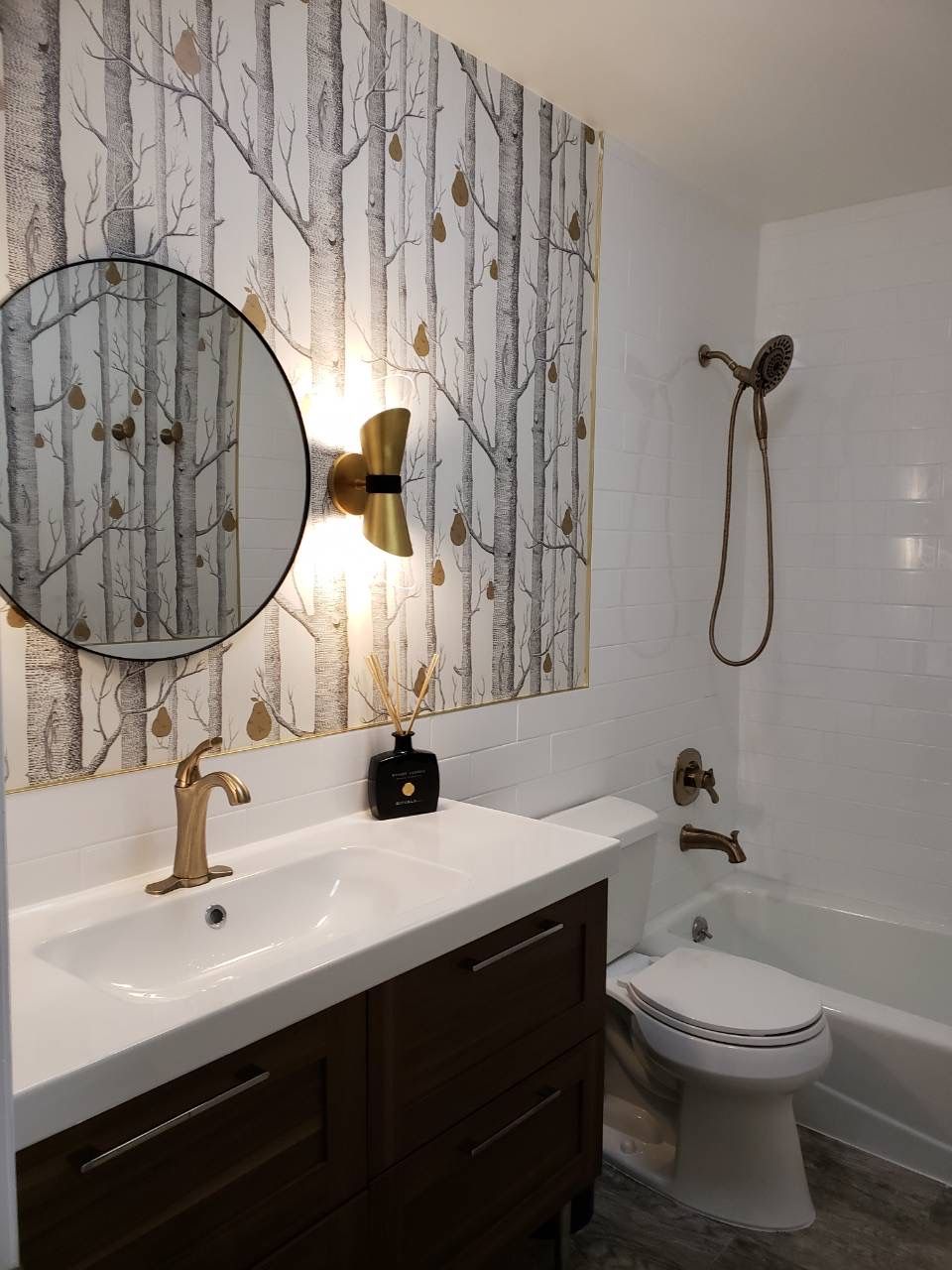 Bathroom wall with tree-pattern wallpaper, round mirror, and brass wall sconces