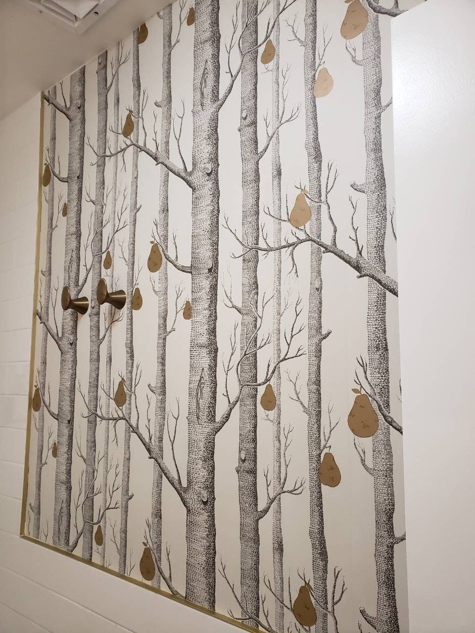 Bathroom with tree-pattern wallpaper, round mirror, brass sconce, and shower fixture