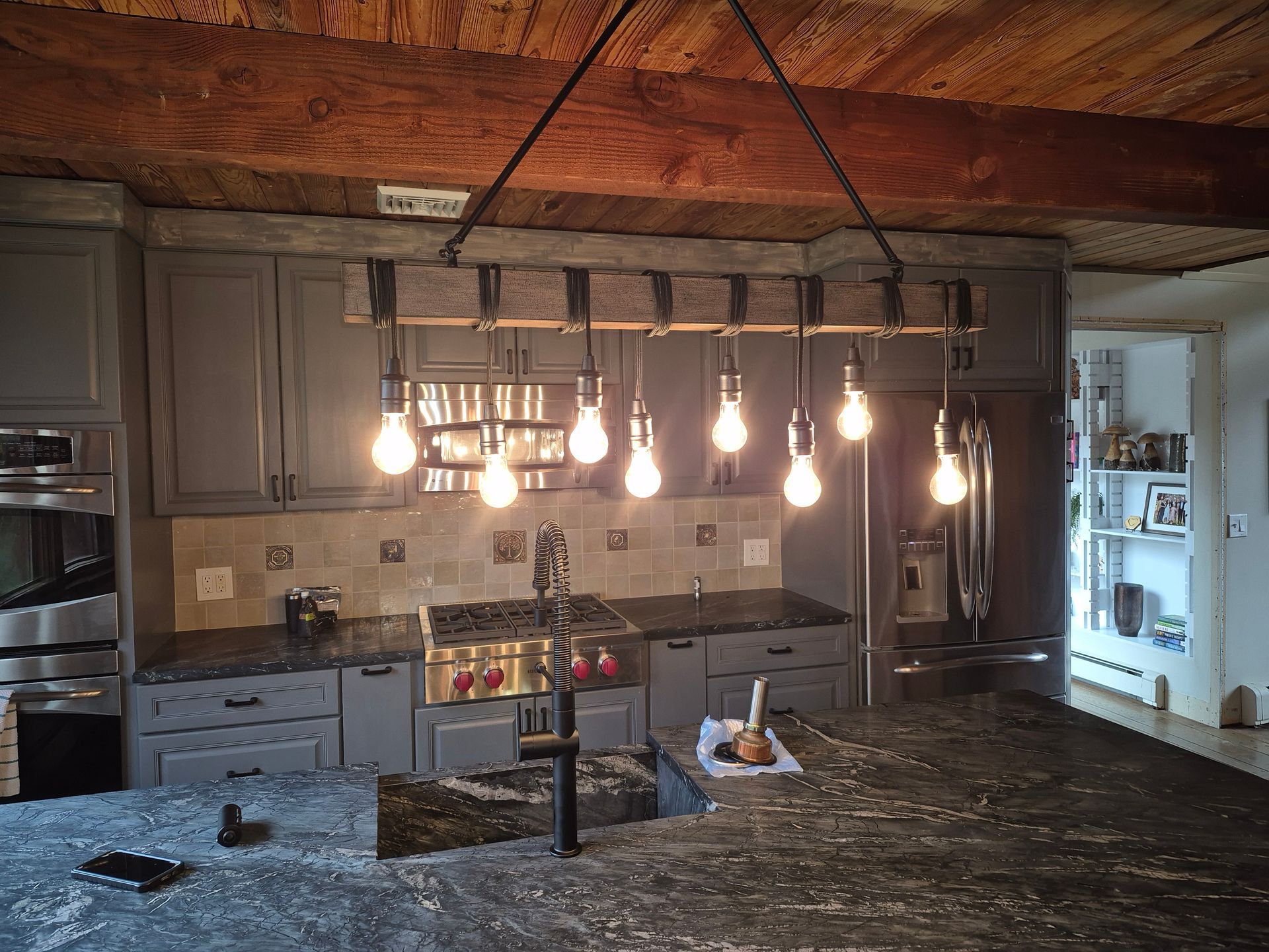 Rustic kitchen with wood ceiling, gray cabinetry, tile backsplash, and hanging Edison bulb light fixture