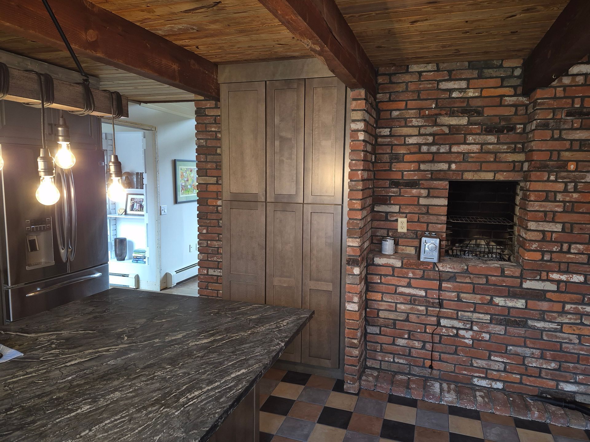 Rustic kitchen with brick wall, wood cabinetry, stone countertop, and exposed wood ceiling beams