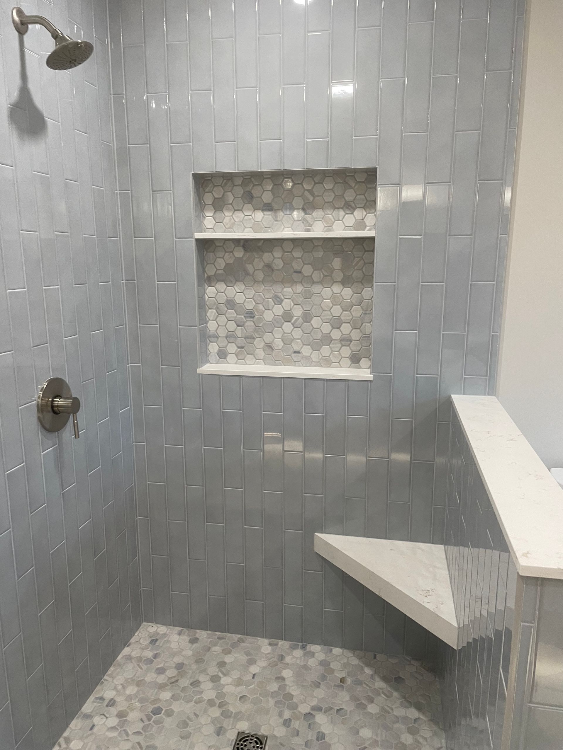 Gray tile shower wall with built-in niche, handheld shower fixture, and polished finish