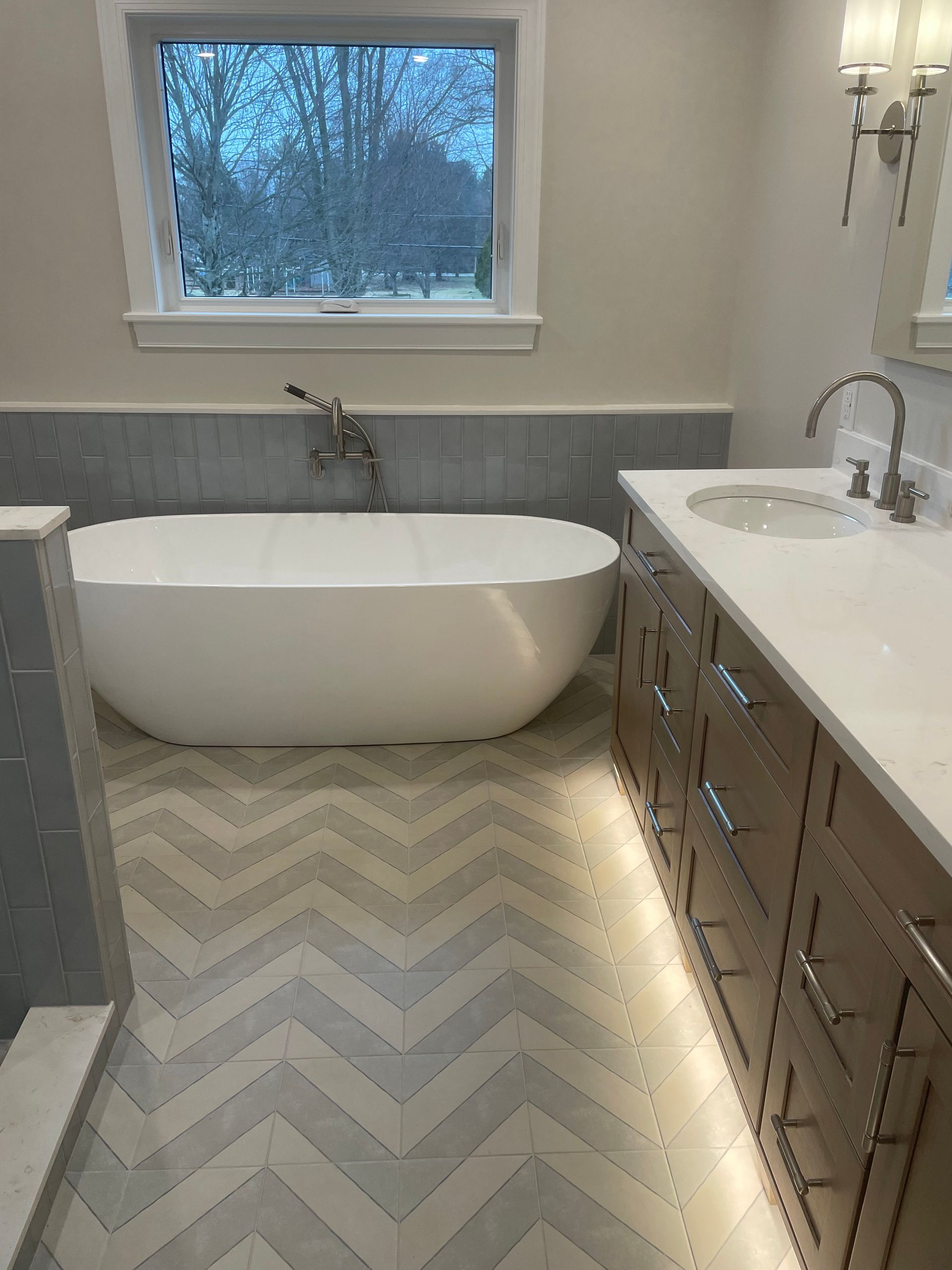 Bright bathroom with freestanding tub, gray tile wainscoting, window, and wall sconce