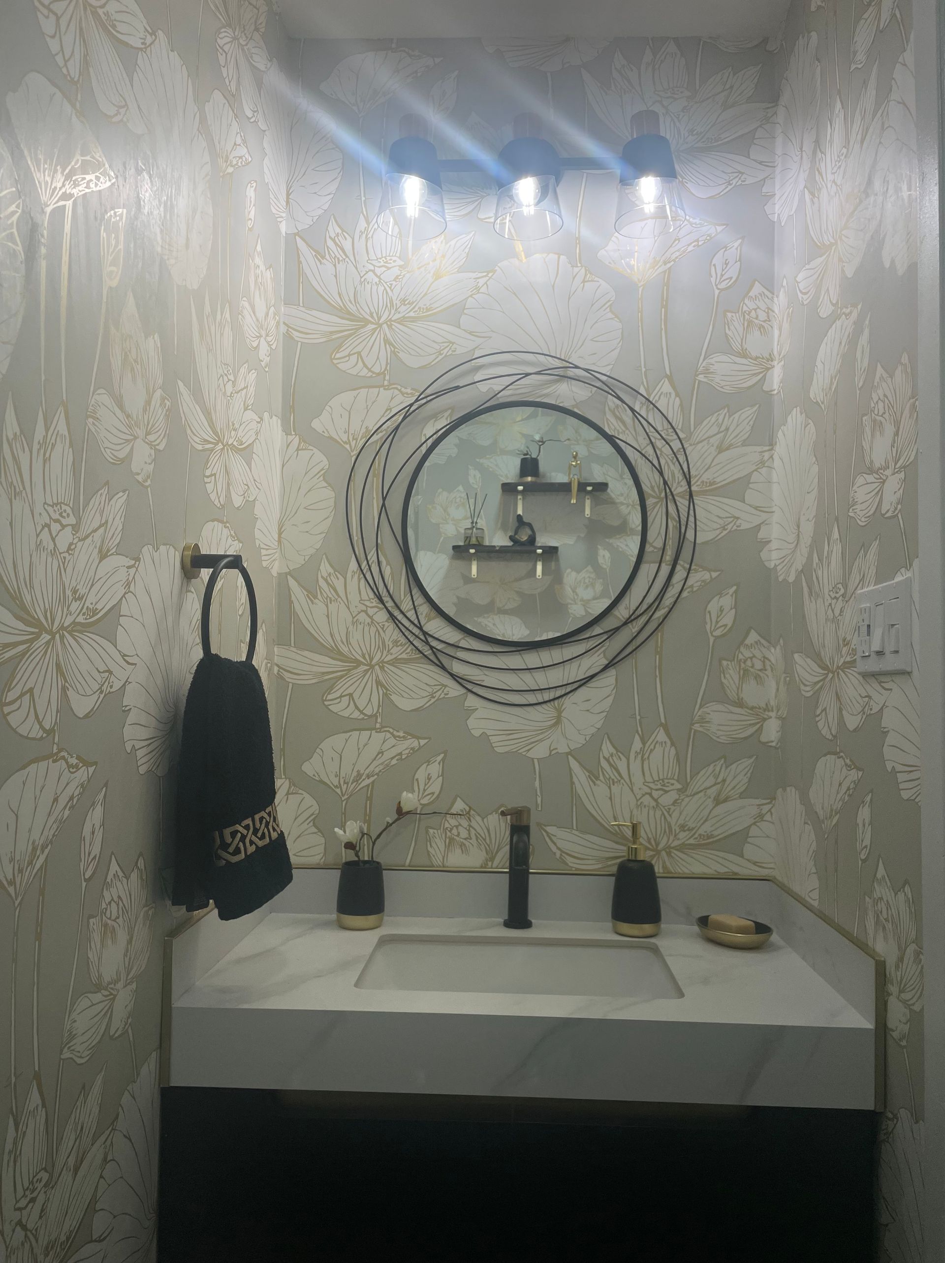 Powder Room vanity wall with floral wallpaper, round mirror, and three-light fixture