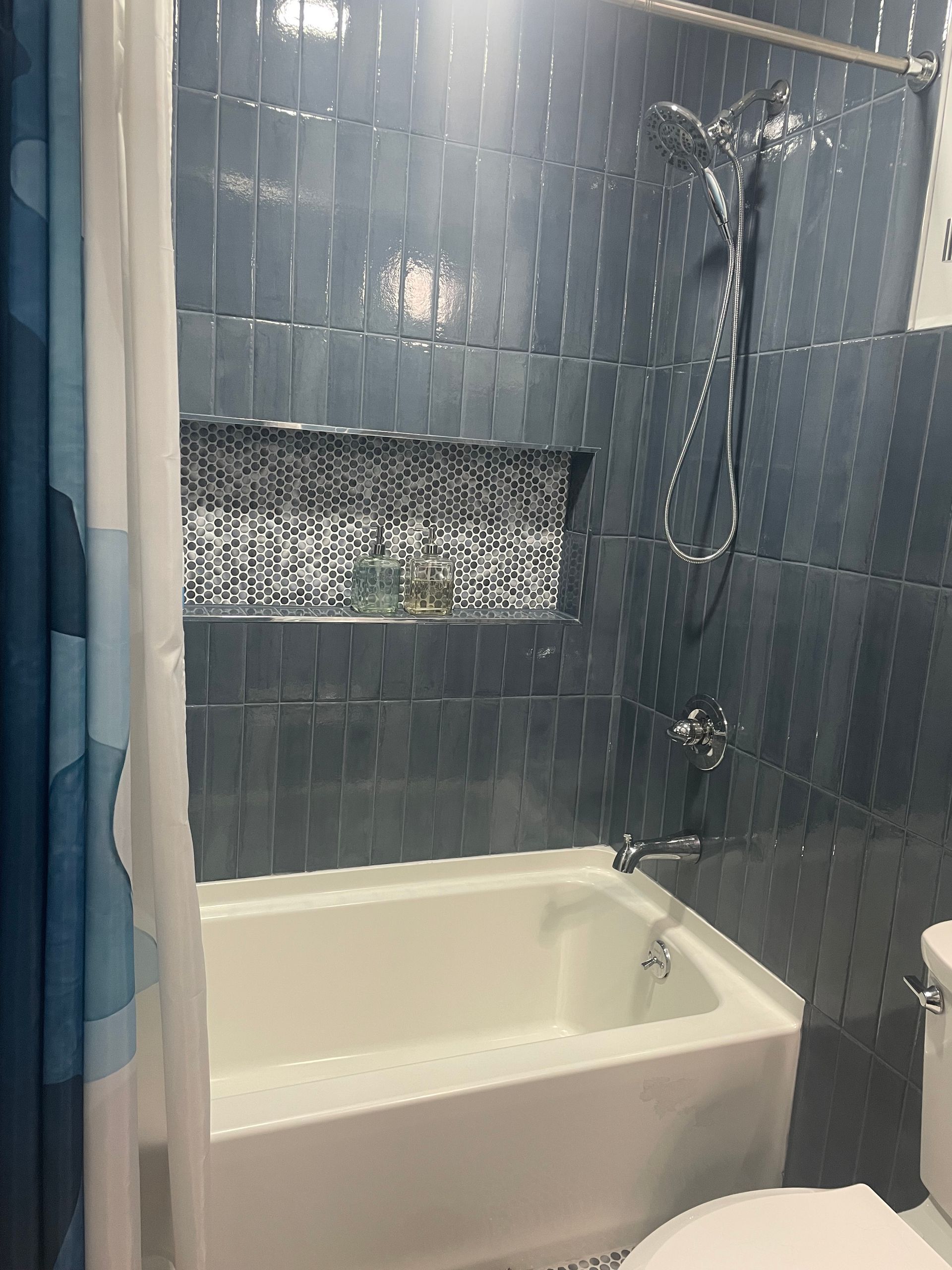 Blue tile shower with glass enclosure, handheld shower fixture, and built-in niche