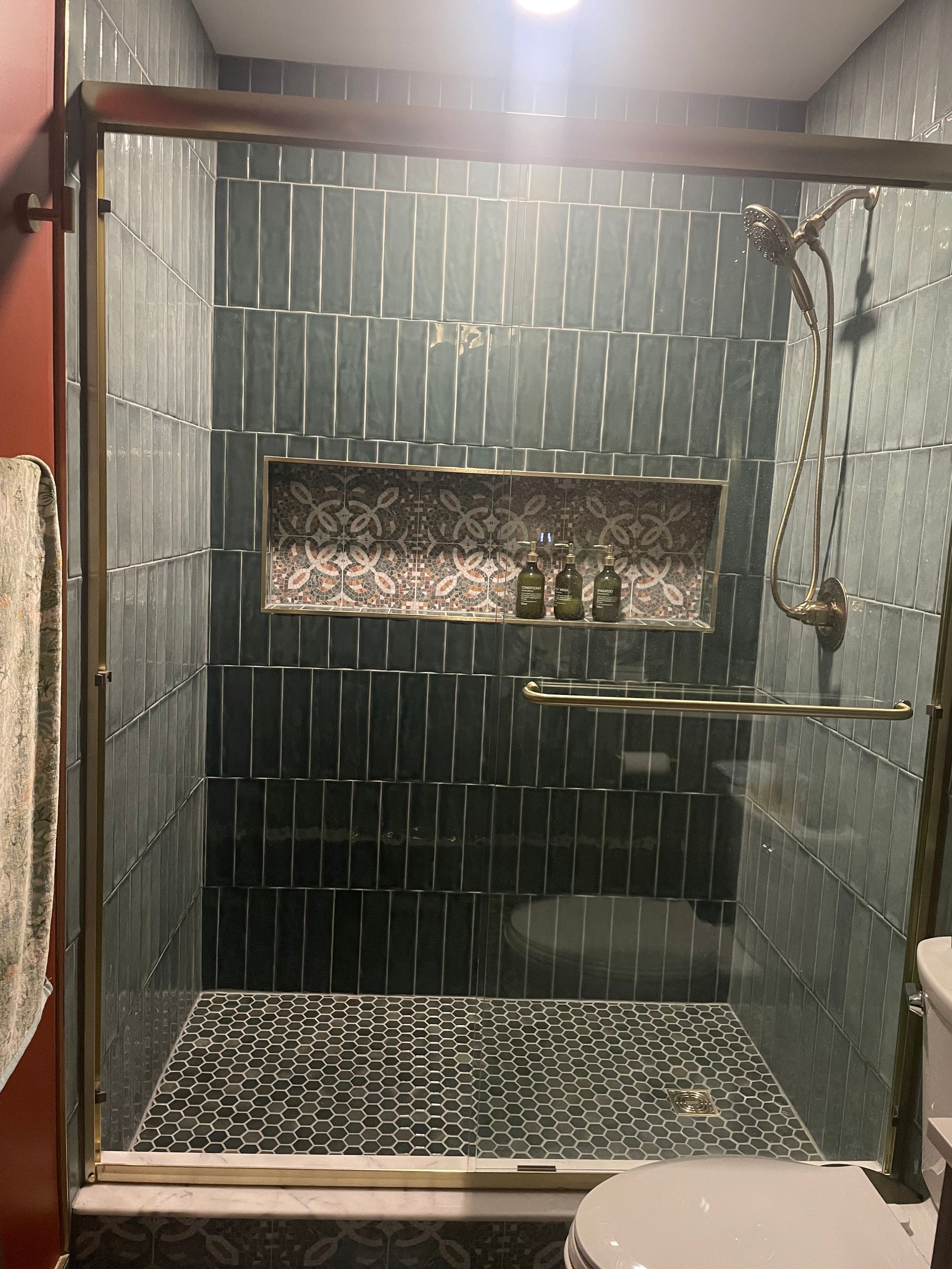 Shower with gray vertical tile, patterned accent niche, glass enclosure, and handheld fixture