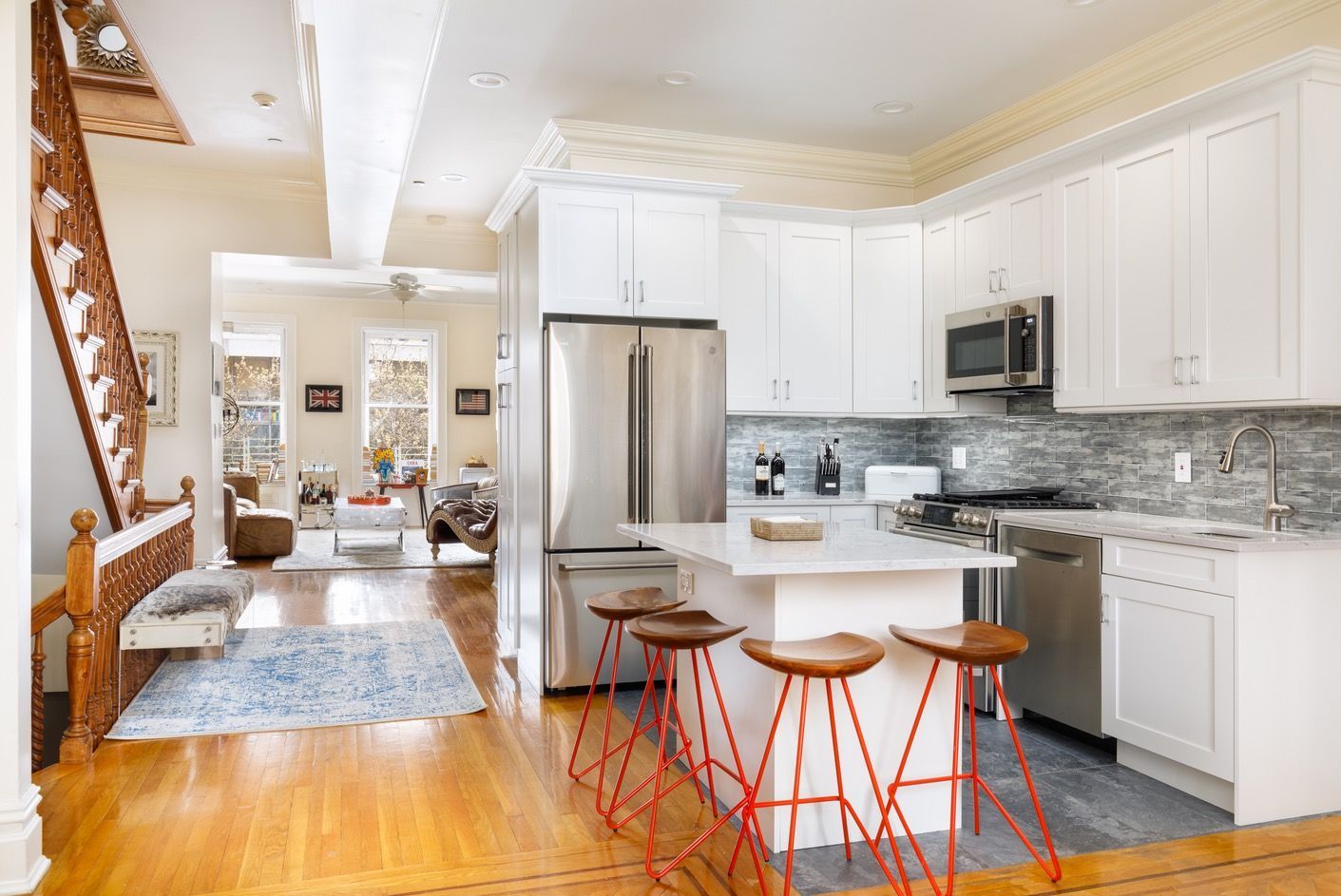 Open kitchen with white cabinets, stainless refrigerator, island seating, and staircase view
