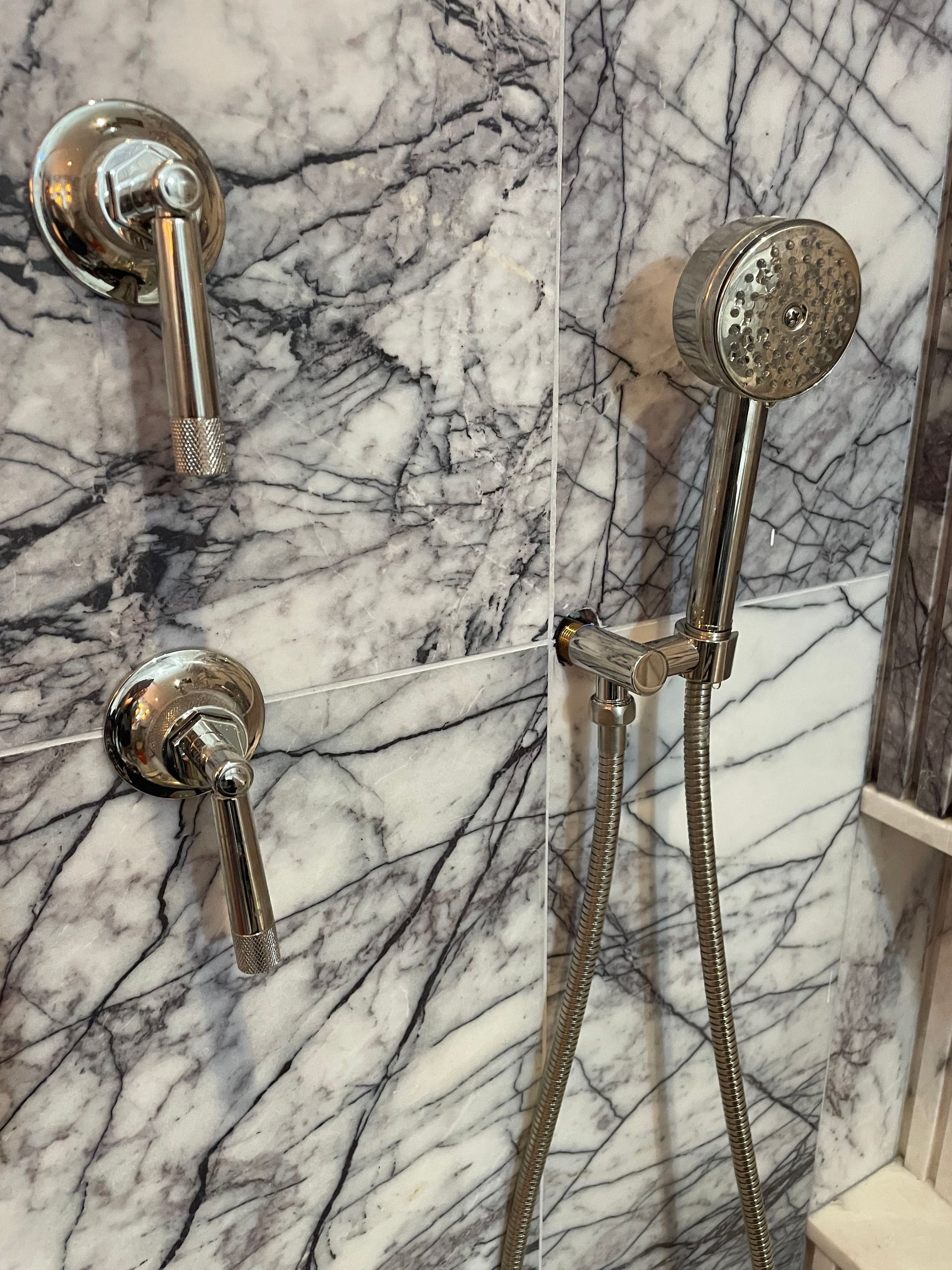 Close-up of shower fixtures mounted on dramatic gray and white marble tile