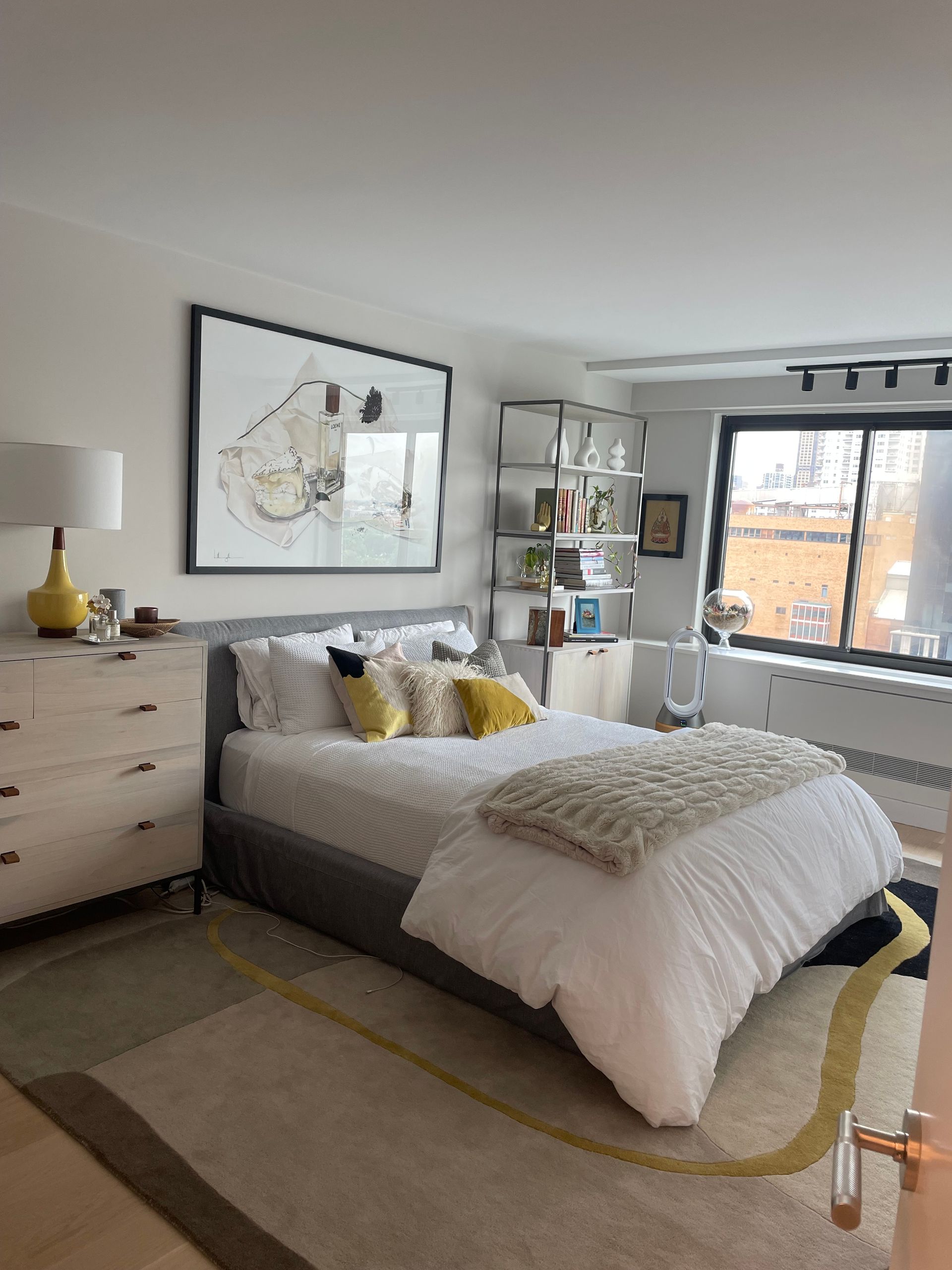 Bright  bedroom with framed artwork, floor lamp, shelving, and track lighting