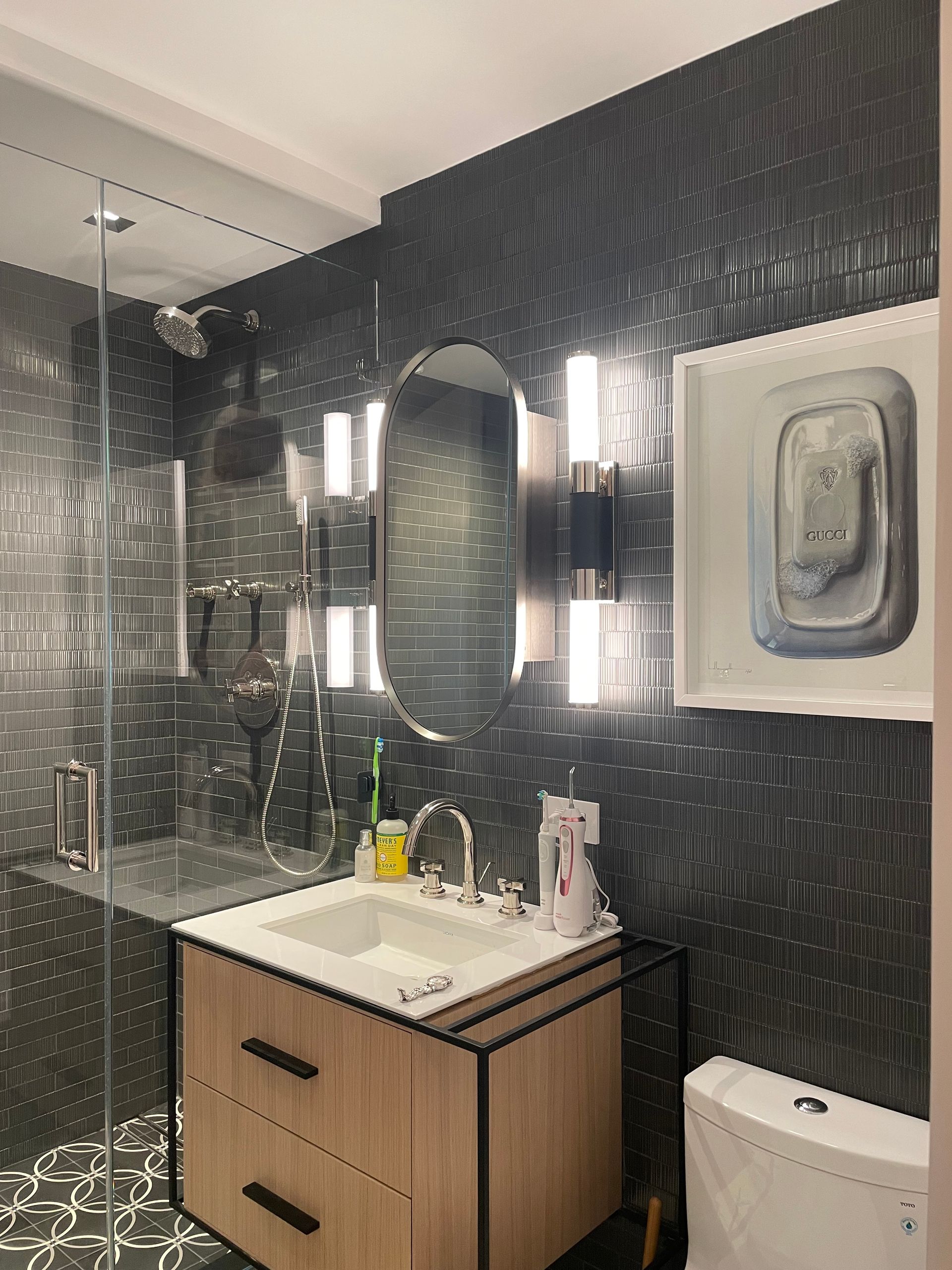 Dark tiled bathroom with glass shower, arched mirror, wall sconces, and modern fixtures