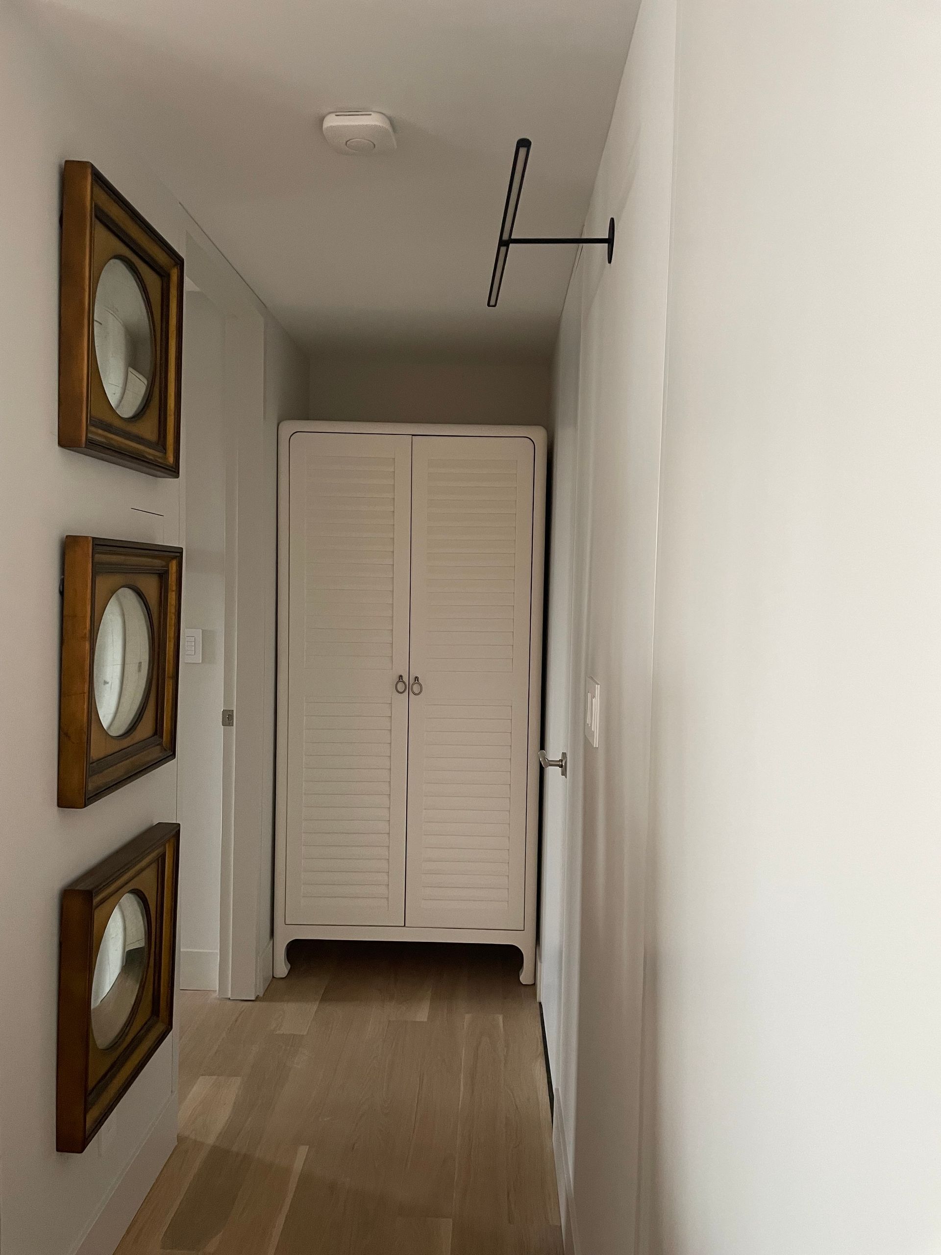 Minimal hallway with white walls, closet doors, mirror, and modern ceiling light