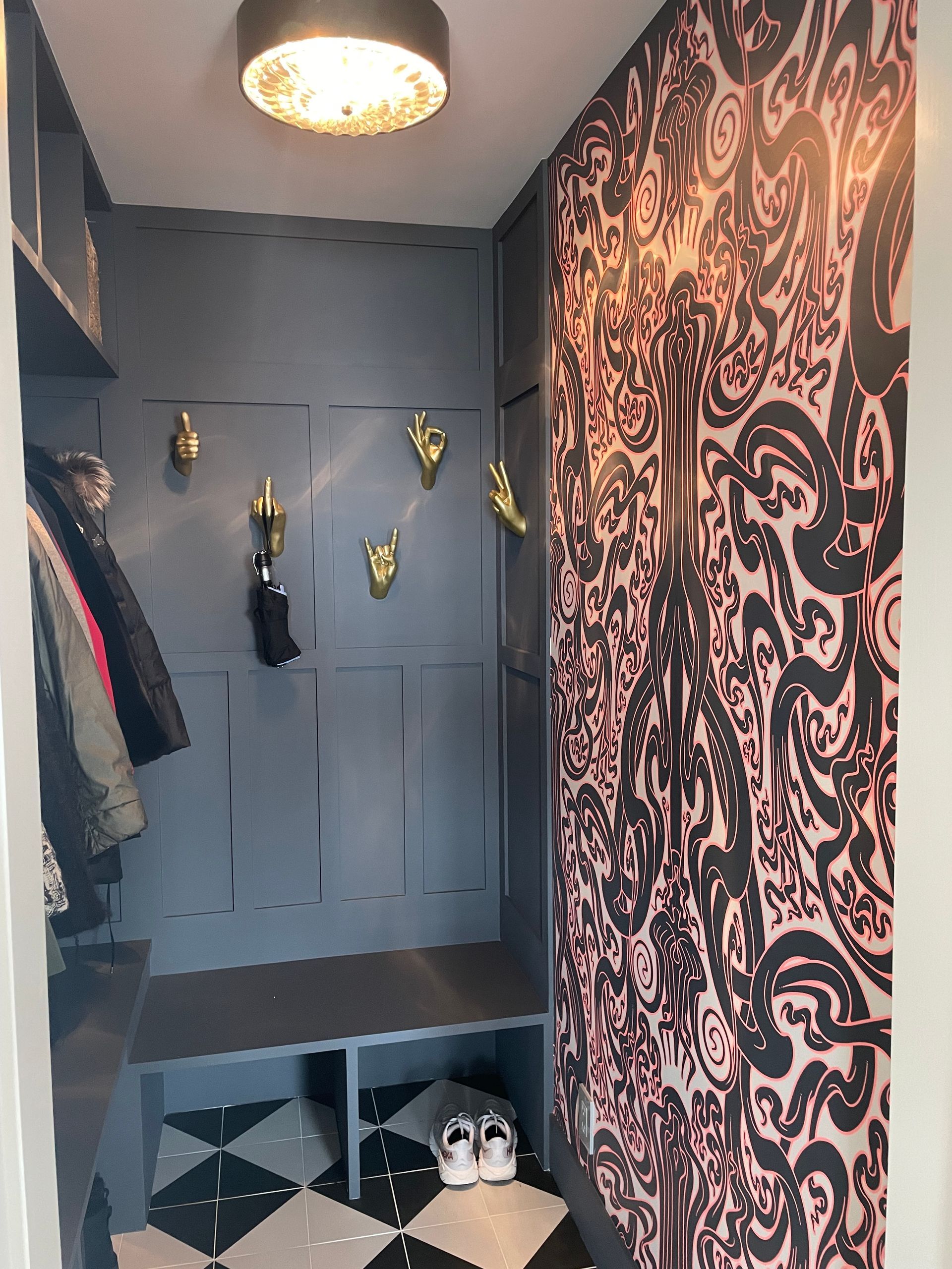 Moody interior corner with patterned wallpaper, wall hooks, and ceiling light