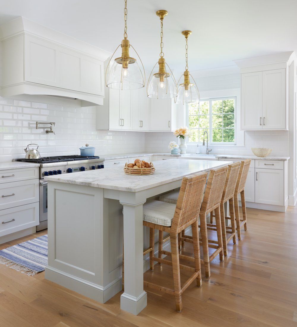 Bright white kitchen with subway tile backsplash, brass pendant lights, and stainless range