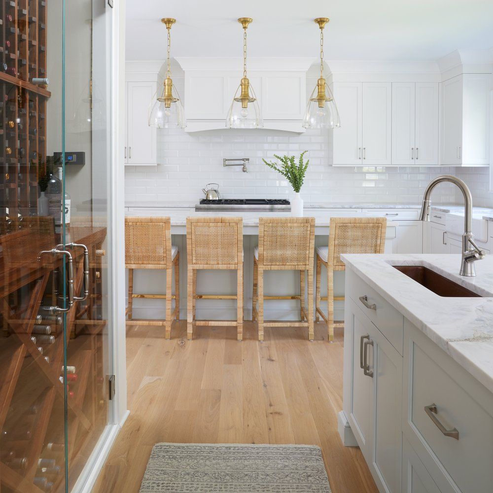 White kitchen island with woven counter stools, brass pendant lights, and subway tile backsplash