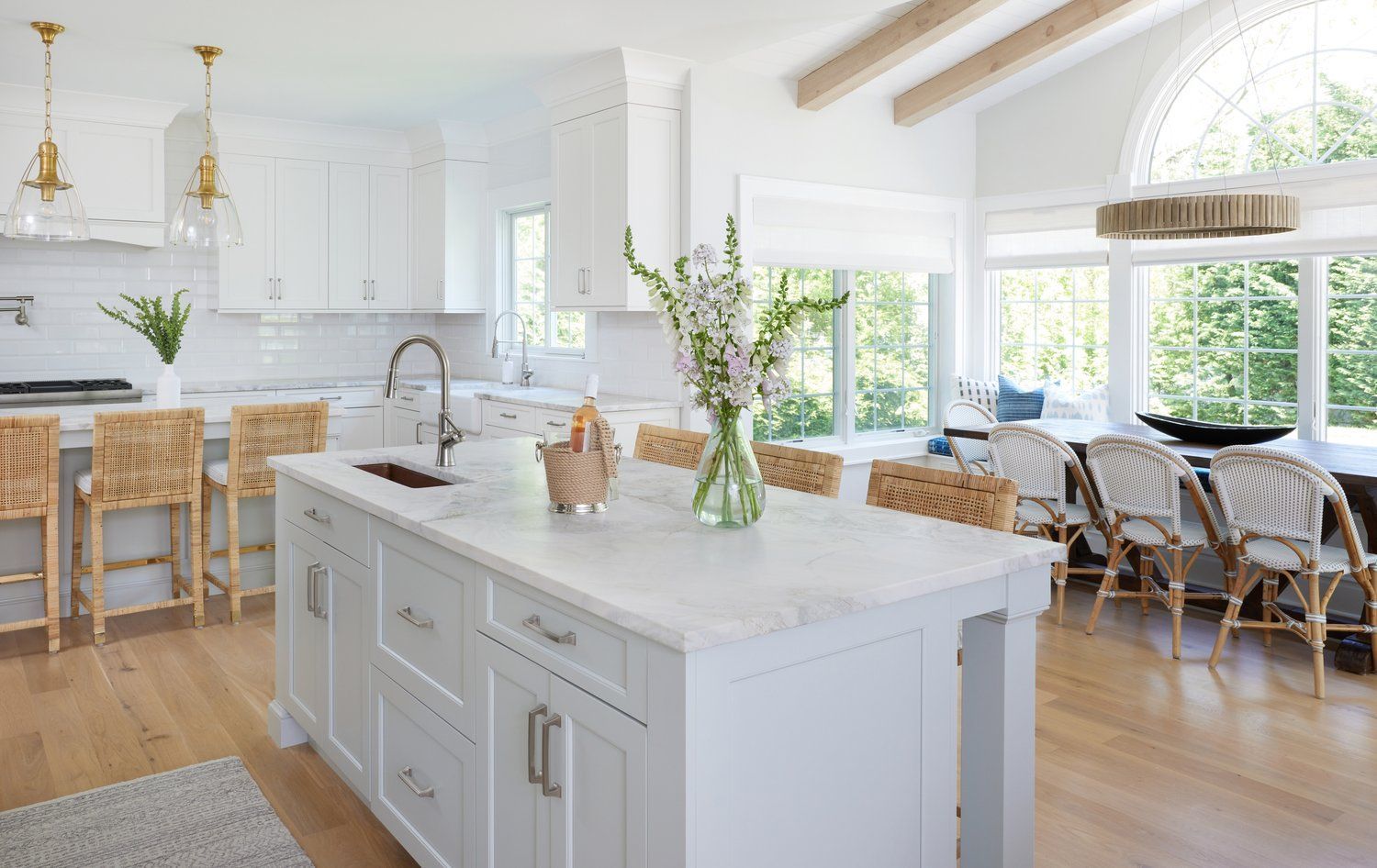Country chick White kitchen with large island, wood beams, arched window, and natural light