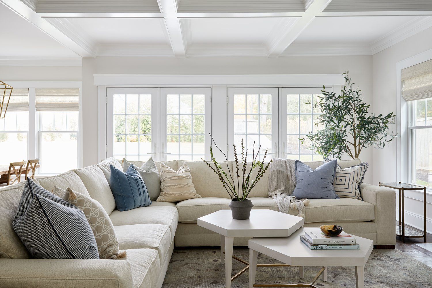 Light-filled sitting room with coffered ceiling, white sectional, round coffee table, and tall windows