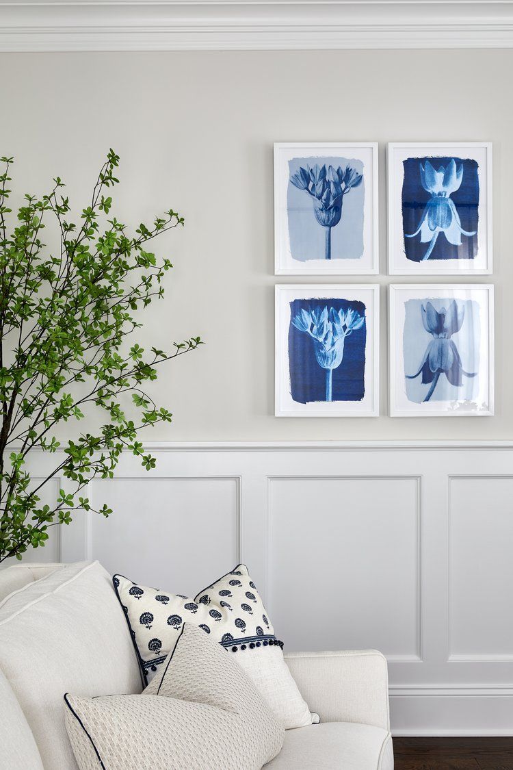Blue botanical artwork on a light wall with greenery in the foreground with traditional upholstere white armchair 