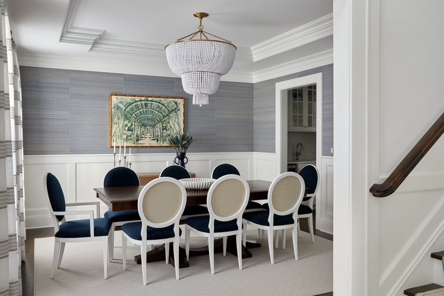 Elegant  traditional dining room with blue wallcovering, white dining chairs, round table, and beaded chandelier
