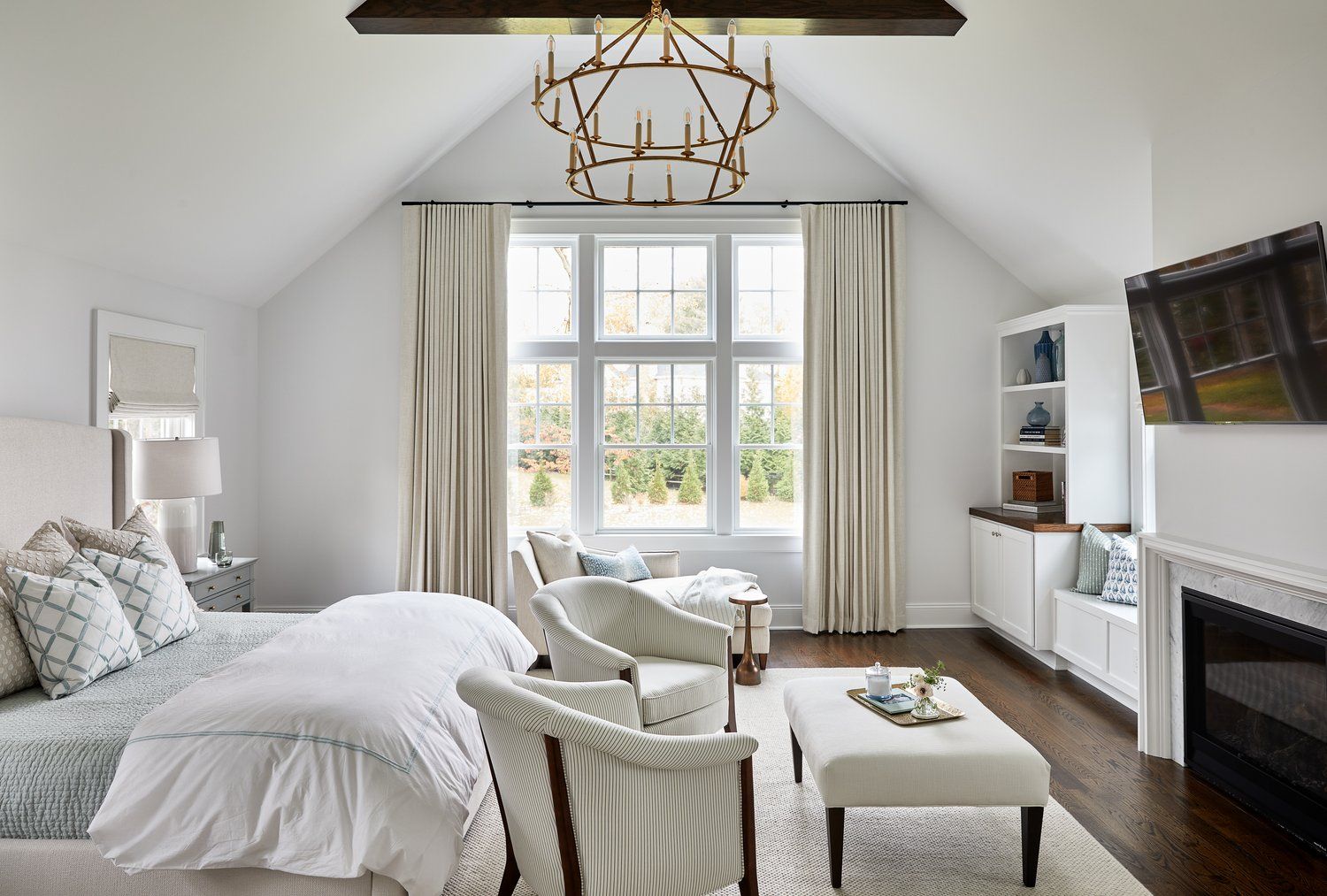 Bright  bedroom with vaulted ceiling, chandelier, sofa, fireplace, and large window