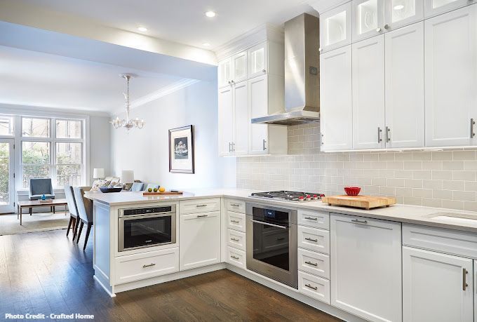 Bright white kitchen with stainless range hood, subway tile backsplash, oven, and open dining area