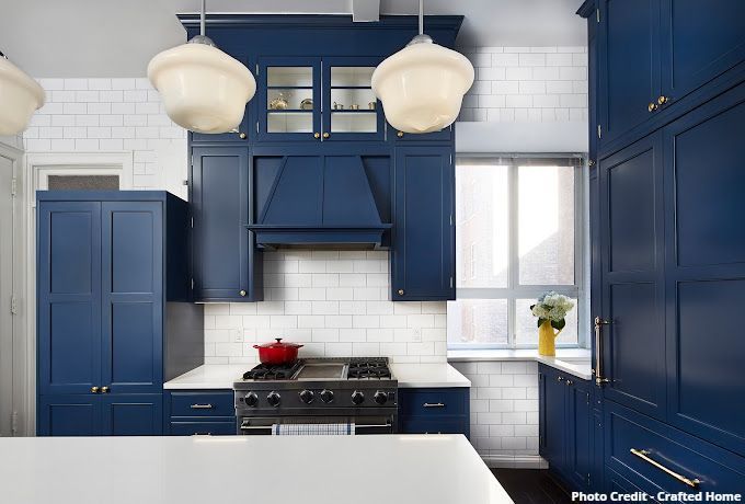 Blue kitchen with range hood, white subway tile backsplash, brass hardware, and globe pendants