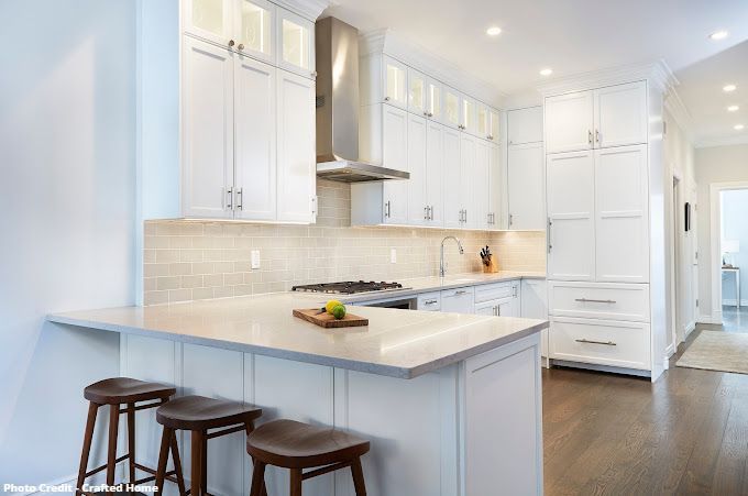 White kitchen with island seating, stainless range hood, subway tile backsplash, and bright lighting