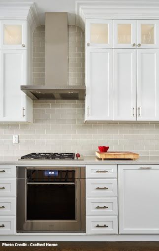 White kitchen cabinets with frosted glass doors, stainless range hood, and tile backsplash