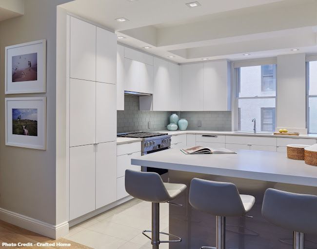 Modern white kitchen with island, waterfall countertop, tall cabinets, and city window view