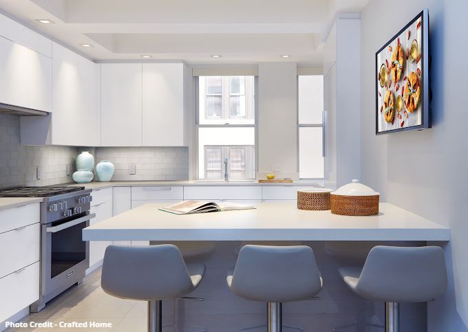 Bright kitchen with white island, blue chairs, framed artwork, and city window view