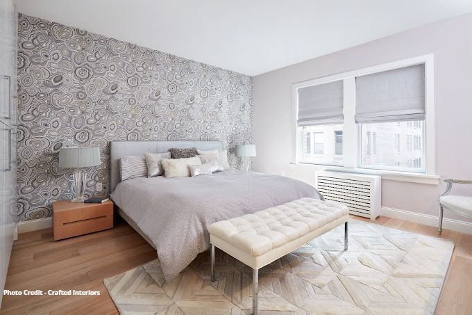 Elegant bedroom with patterned wallpaper, upholstered bench, neutral bedding, and window shades