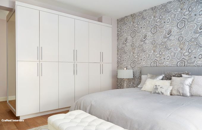 Bright bedroom with white wardrobes, patterned accent wall, bedside lamps, and neutral bedding