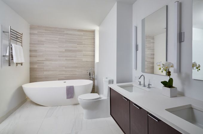 Bright bathroom with freestanding tub, double vanity, wall-mounted toilet, and neutral tile