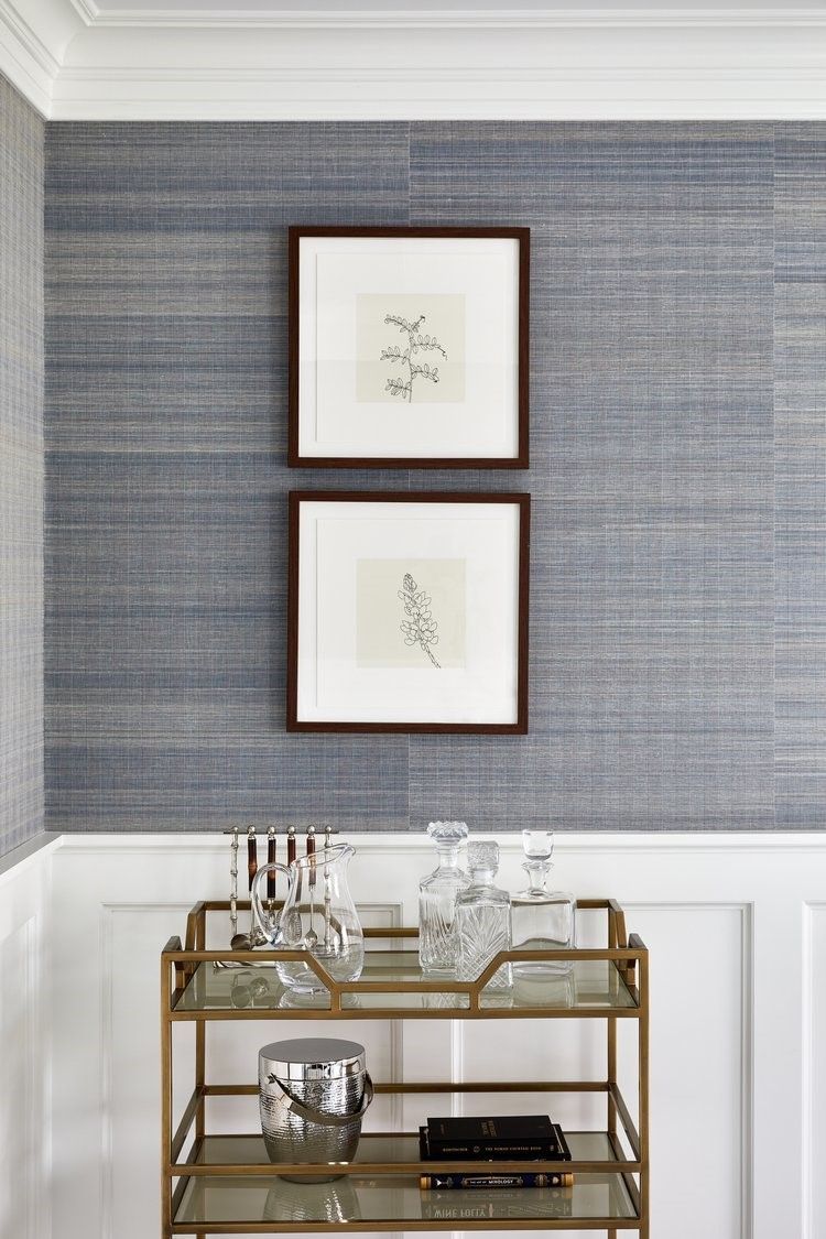 Framed artwork displayed on textured blue wallcovering with classic crown molding and bar cart