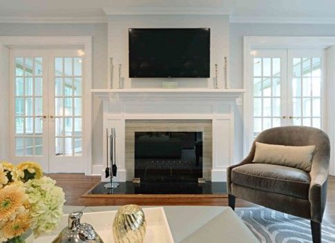 Classic living room with white fireplace, wall-mounted TV, French doors, and armchair