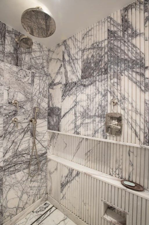 Close-up of marble bathroom wall with round mirror and glass shower enclosure