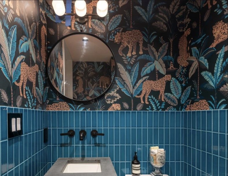 Bold Powder room with tropical wallpaper, round mirror, blue tile wainscoting, and globe lighting