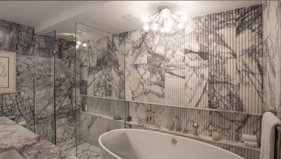 Fluted Lilah Marble bathroom with glass shower, freestanding tub, patterned stone walls, and ceiling light