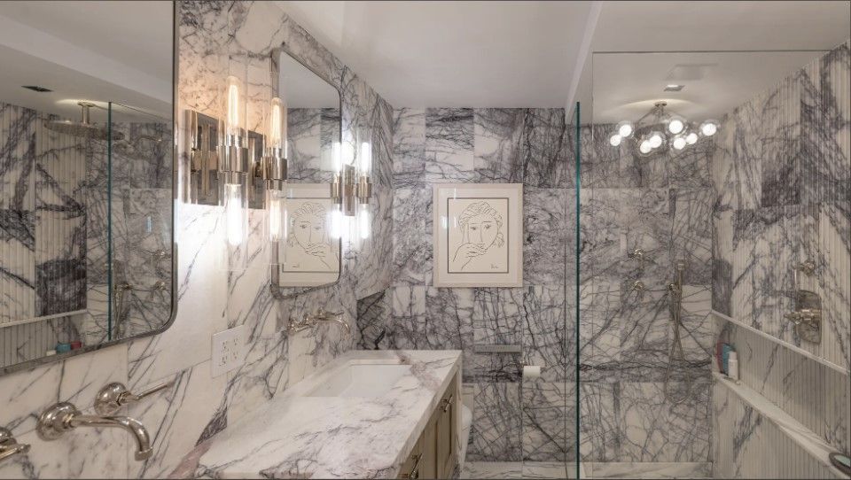 Elegant Lilah marble bathroom with mirrored vanity wall, chandelier, and framed artwork