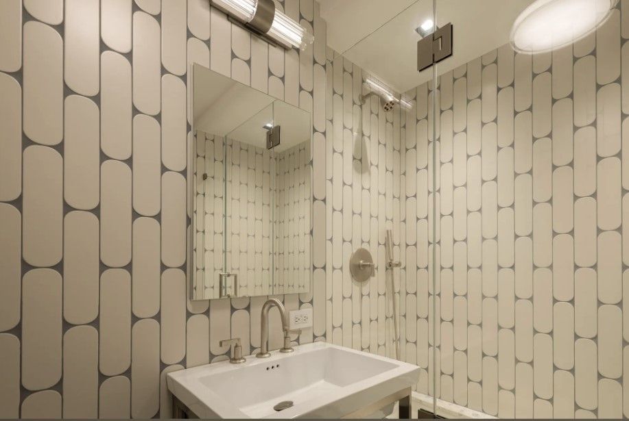 White bathroom with geometric wall tile, glass shower, vanity, and wall lighting