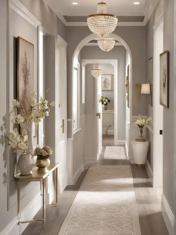 Elegant hallway with arched doorway, chandelier, framed artwork, and neutral walls