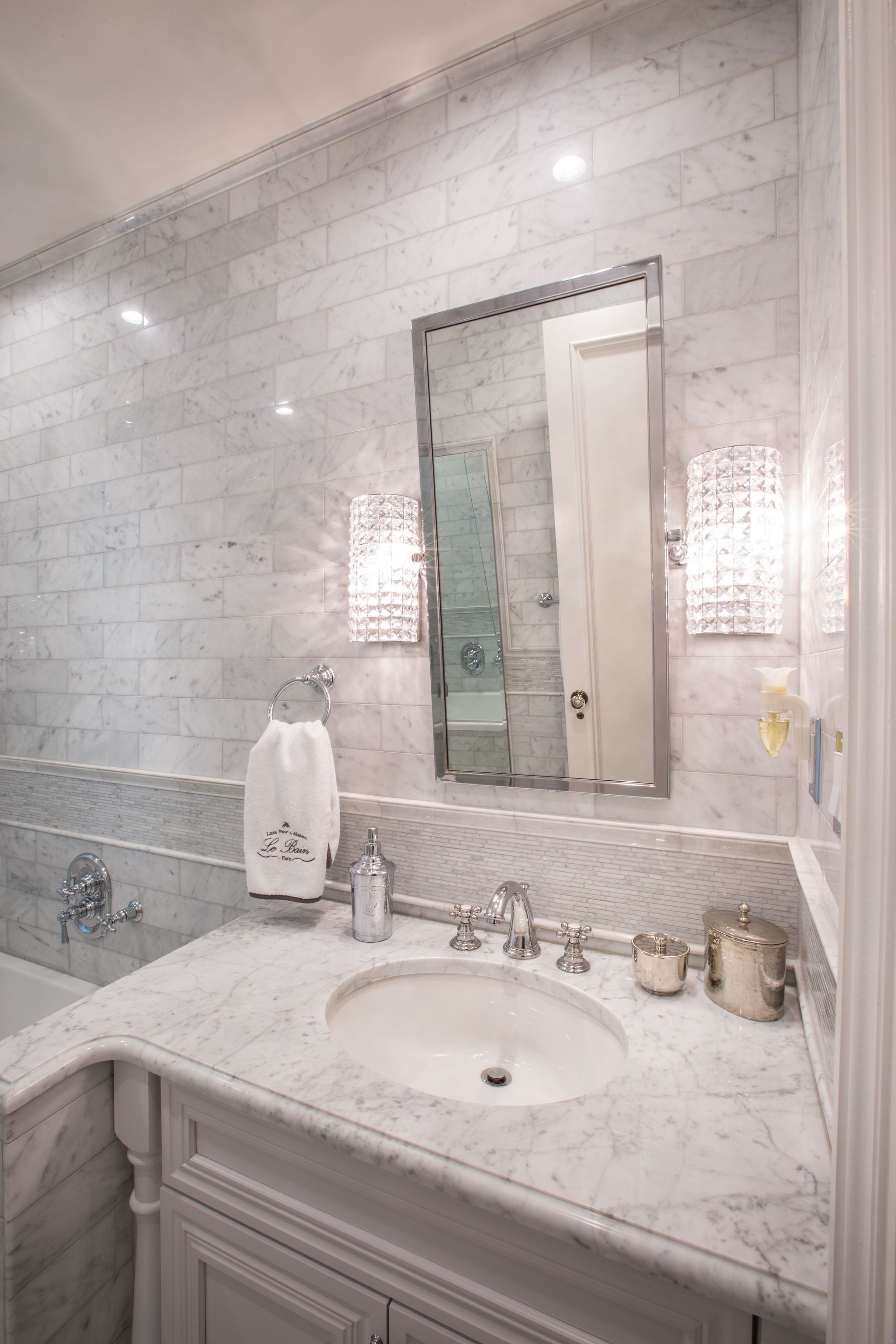 Close-up of white marble bathroom wall with mirror, tile detail, and polished finish