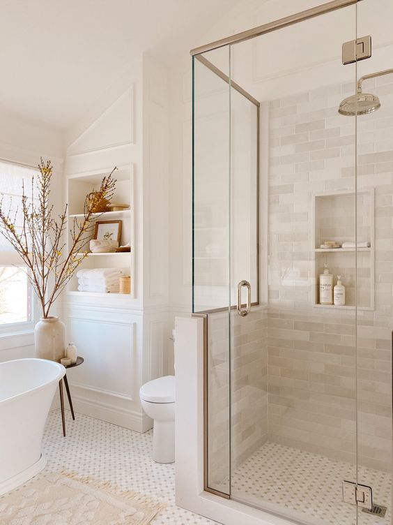 Bright bathroom shower with glass enclosure, white tile, and brass fixture